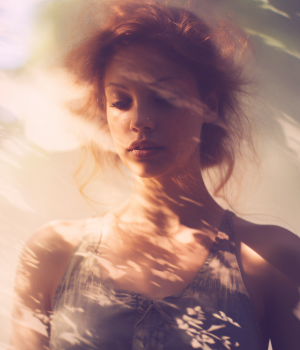 Eine Nahaufnahme einer Frau, die in einer meditativen Pose sitzt und die sanften Rauchschwaden eines Räucherstäbchens oder -kräutels aufnimmt. Die gedämpfte Beleuchtung und die unscharfen Hintergründe tragen zur besinnlichen Stimmung bei.