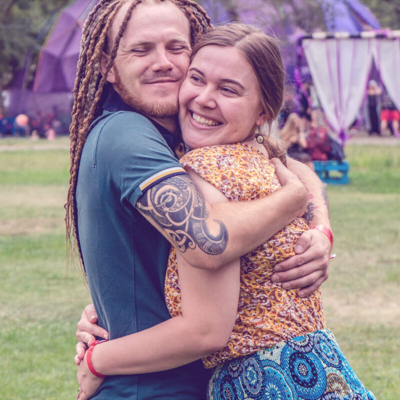 Ein junges Hippie-Paar umarmt sich lächelnd vor einem Festival-Hintergrund