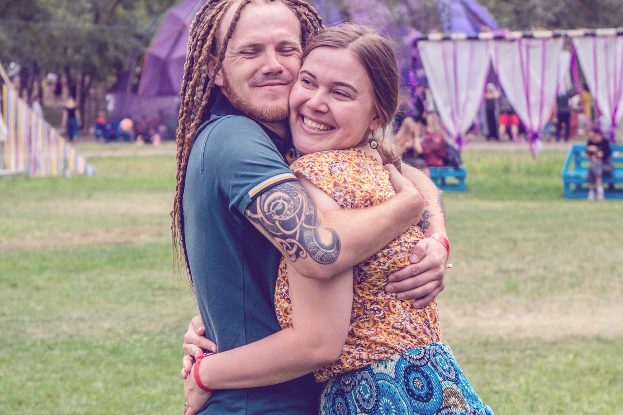 Ein junges Hippie-Paar umarmt sich lächelnd vor einem Festival-Hintergrund